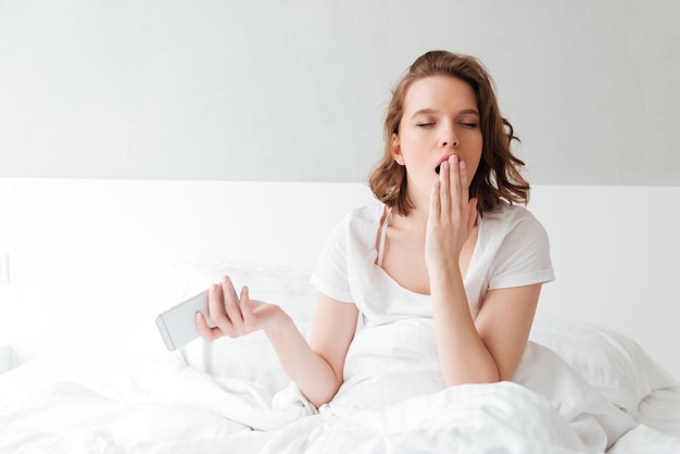 Bored young woman in bed indoors with eyes closed yawning