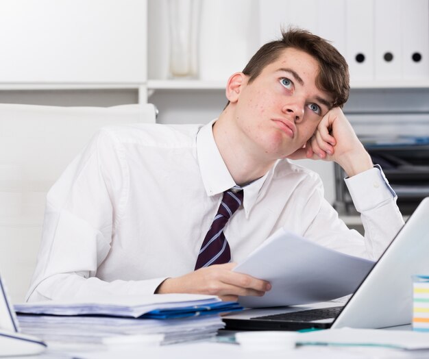 Boring teenager reading documents near the laptop