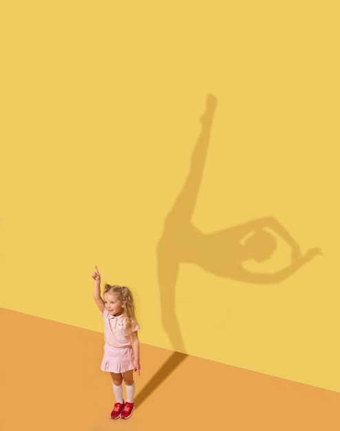 Free photo born to cause emotions. childhood and dream concept. conceptual image with child. shadow on studio wall is painted by me. little girl want to become ballerina, ballet dancer, artist in theatre.