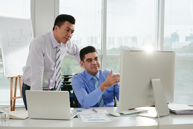 Boss checking work done by his subordinate showing the results on the computer screen