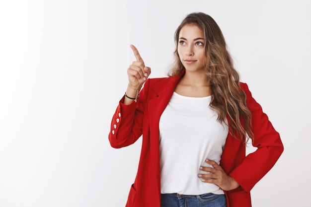 Bossy good-looking successful young modern female entrepreneur giving directions employees pointing index finger copy space looking upper left corner serious confident gaze, white wall