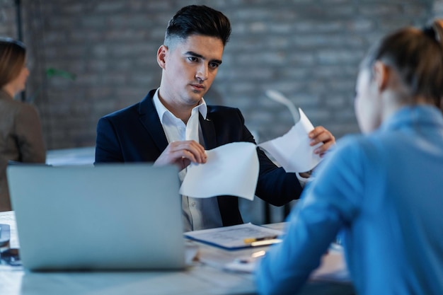 Bossy manager tearing apart business reports in front of his female colleague in the office