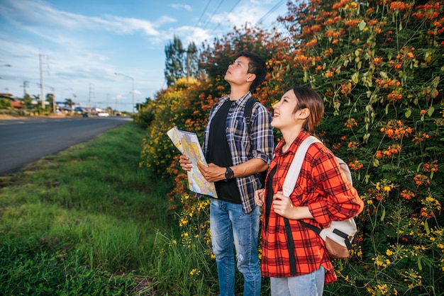 Both male and female tourists carry a backpack standing at a flower garden. And look to the top