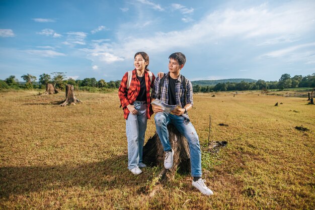 Both male and female tourists carry a backpack standing on the lawn. And look to the side.