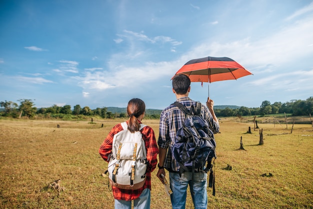 Both male and female tourists carry a backpack standing on the lawn.