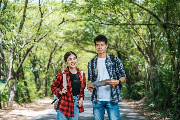 Both male and female tourists stand to see the map on the road.