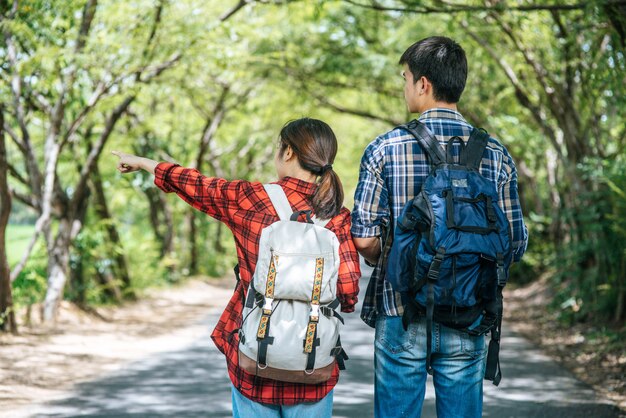 Both male and female tourists stand to see the map on the road.