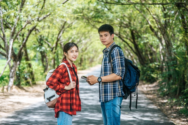 Both male and female tourists stand to see the map on the road.