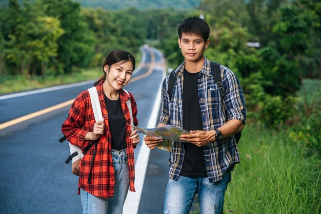 Туристы мужского и женского пола стоят, чтобы увидеть карту на дороге.