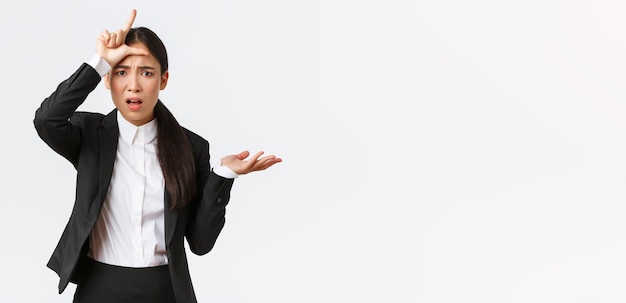 Бесплатное фото Обеспокоенная и раздраженная азиатская деловая женщина ругает сотрудника за неудачу, показывая жест неудачника и поднимая руку в тревоге, не может понять, почему так глупо жалуется на белом фоне