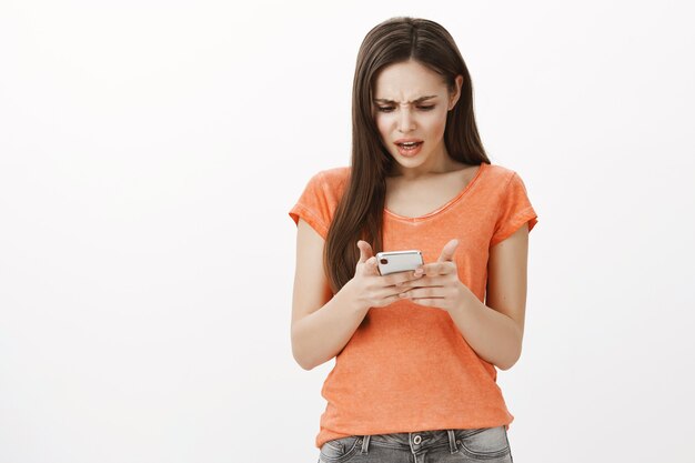 イライラした携帯電話を見て困惑し、混乱しているブルネットの少女