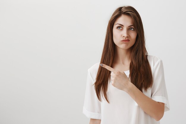 Bothered and disappointed woman pouting with regret as pointing upper left corner