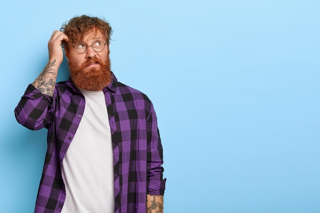 Free photo bothered thoughtful bearded man with curly ginger hair, scratches head, thinks something over