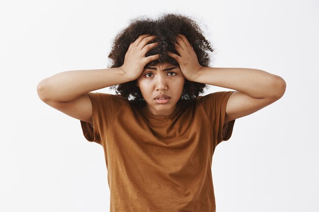 bothered and tired depressed african american woman with afro hairstyle feeling annoyed and exhausted with louds of troubles on head frowning holding hands on hair