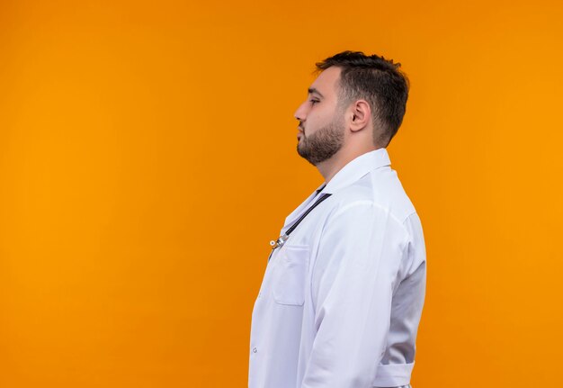 Обеспокоенный молодой бородатый мужчина-врач в белом халате со стетоскопом боком