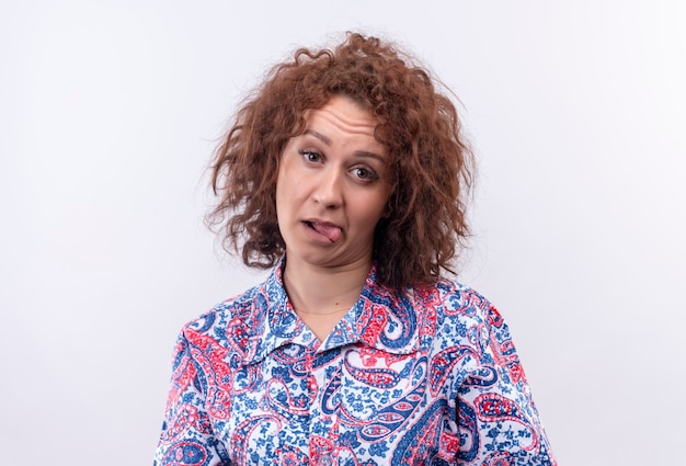 Free photo bothered young woman with short curly hair  in colorful shirt sticking out tongue