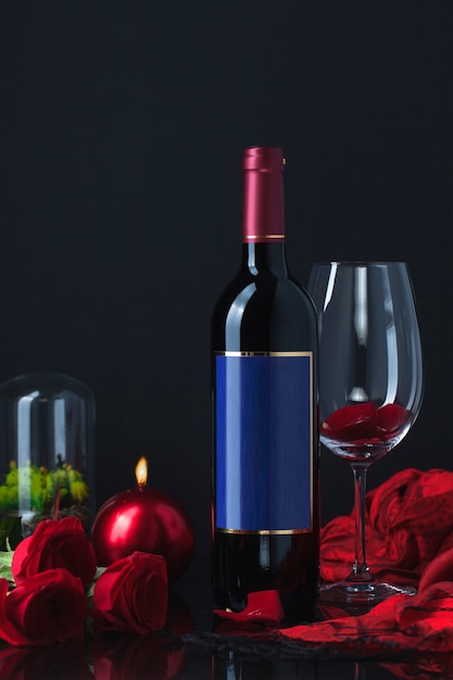 Bottle of alcohol with roses, goblet, candle and scarf