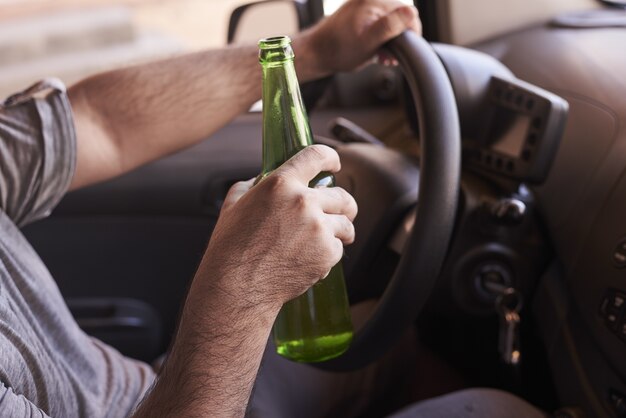 Бутылка пива в руках мужчины за рулем автомобиля в дневное время