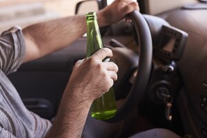 Bottle of beer in a man's hands driving the car during daytime