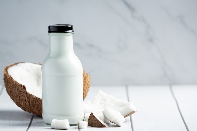 Bottiglia di latte di cocco messo su fondo di legno bianco