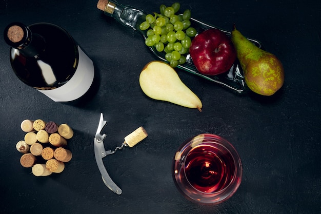 어두운 돌 표면 위에 과일과 함께 병 및 레드 와인 한 잔