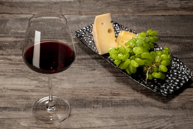 Una bottiglia e un bicchiere di vino rosso con frutta sul tavolo di legno