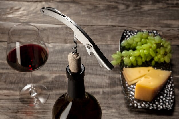 Бутылка и бокал красного вина с фруктами над деревянным столом