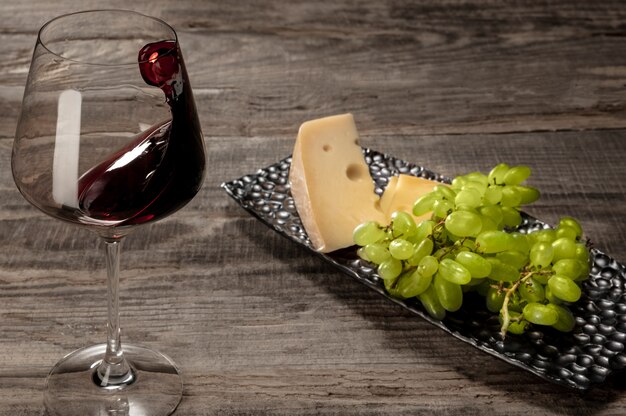 A bottle and a glass of red wine with fruits over wooden