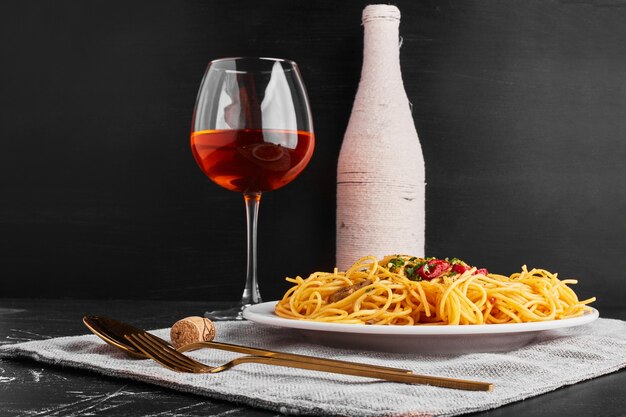 A bottle and glass of rose wine with spaghetti. 