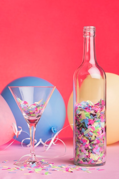 Bottle and glass with confetti on red background