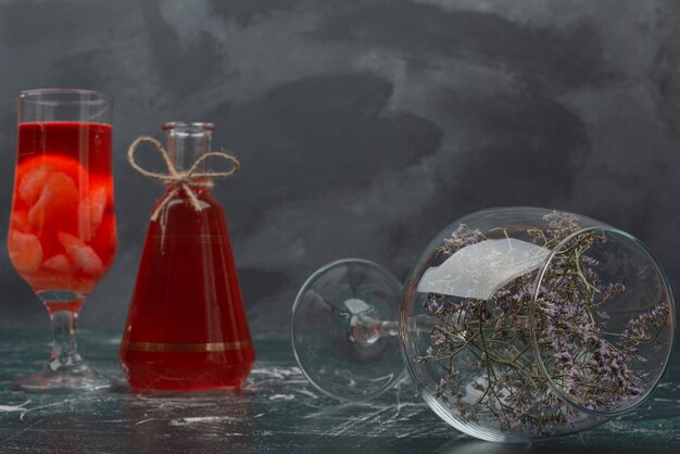 Bottle and glass with juice and glass with flower .