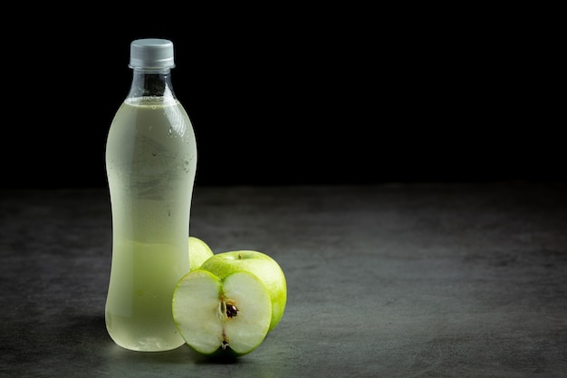 Бутылка полезного сока из зеленого яблока рядом со свежими зелеными яблоками