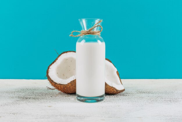 Bottle of milk with divided in half coconuts side view on a white wooden background