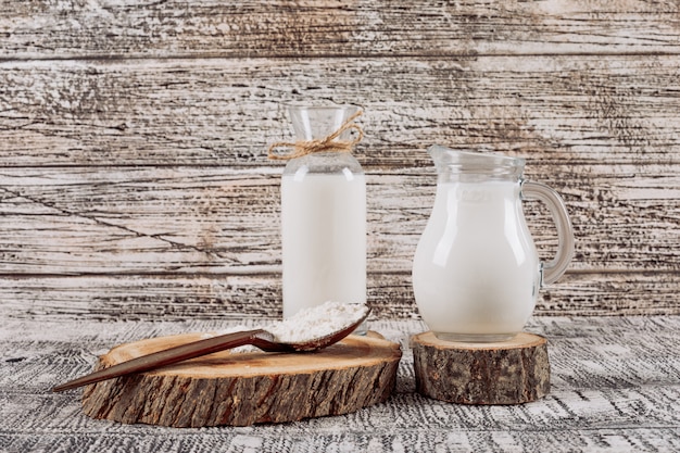 Bottle of milk with milk carafe on wooden slice, wooden spoon high angle view on a white wooden background