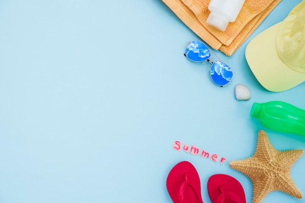 Bottle near towel with starfish and cap with sunglasses and flip flops