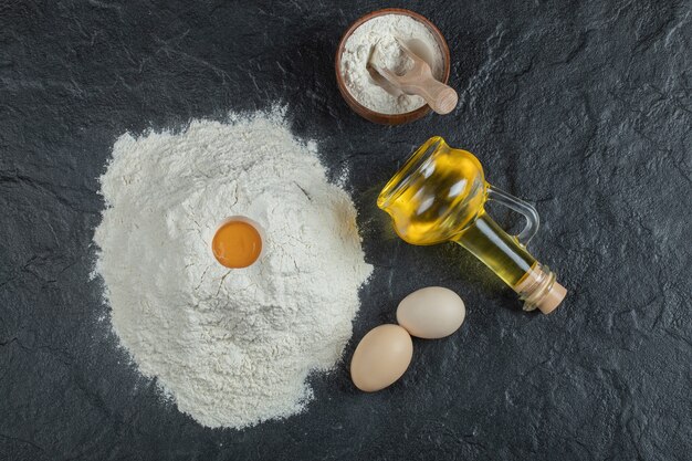 A bottle of oil with wooden bowl of flour and raw yolk. 