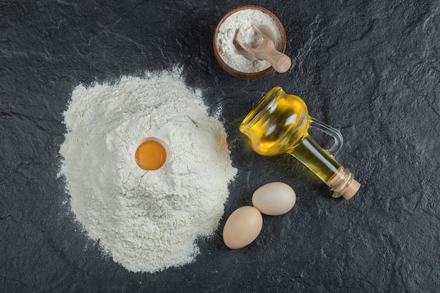 A bottle of oil with wooden bowl of flour and raw yolk. 
