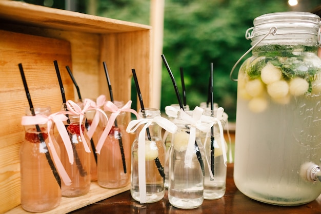 Bottle with fresh lemonade and glasses around it stands on the dinner table in the garden