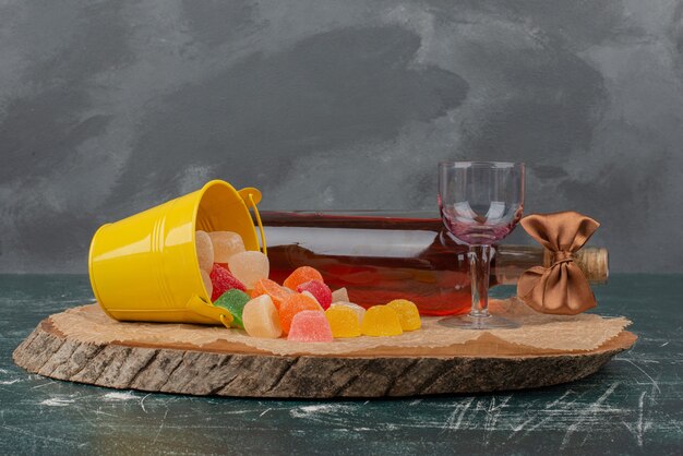 Bottle with glass and jelly candies on wooden board