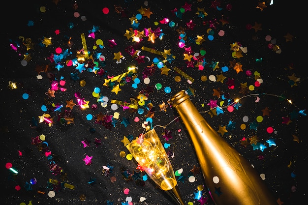 Free photo bottle with glass and spangles on black table