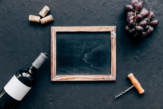 Bottle with grape and corkscrew around blackboard