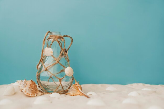 Bottle with rope on sand on blue background