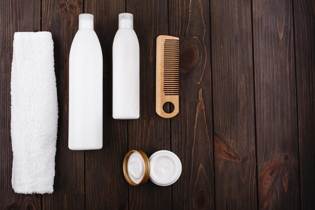 Bottles of shampoo and conditioner lie with towel and comb on wooden table