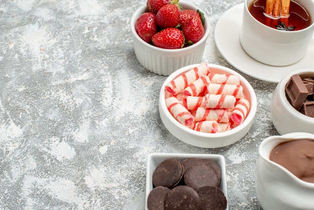 카카오 캔디가 들어있는 하단 가까이보기 그릇 딸기 초콜릿 차와 계피가 들어간 회색 흰색 테이블 오른쪽에 여유 공간이 있습니다.