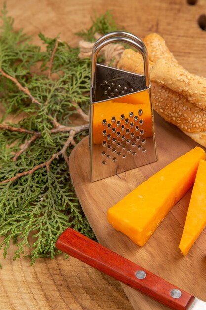 Bottom close view cheese and bread knife small box grater on chopping board pine tree branches on wooden surface