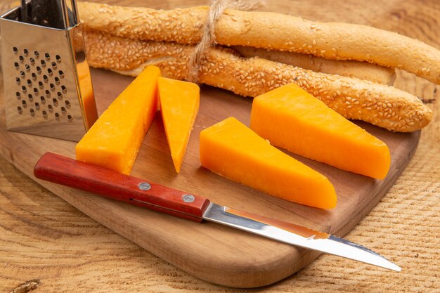 Bottom close view cheese and bread knife small grater on cutting board on wooden surface