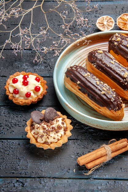 어두운 나무 테이블에 타원형 접시 말린 꽃 지점 타르트와 계피에 하단 닫기보기 초콜릿 eclairs