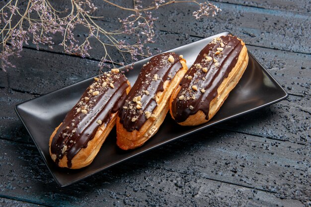 Bottom close view chocolate eclairs on rectangle plate on the dark wooden table