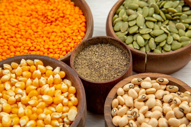 Free photo bottom close view wooden bowls with corn seeds beans pumpkin seeds lentiles black pepper bowl