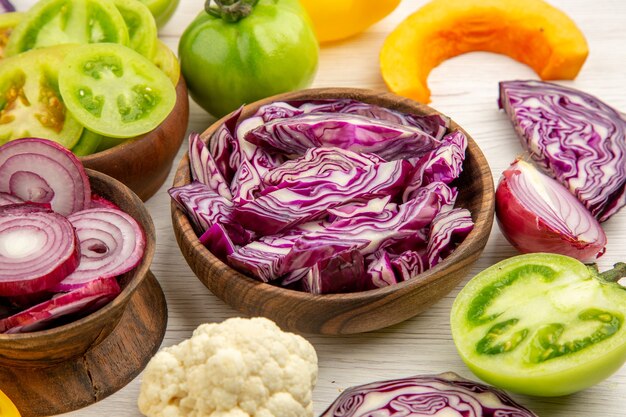 Bottom close view wooden bowls with onion red cabbage green tomato cauliflower cut pumpkin on white wooden table